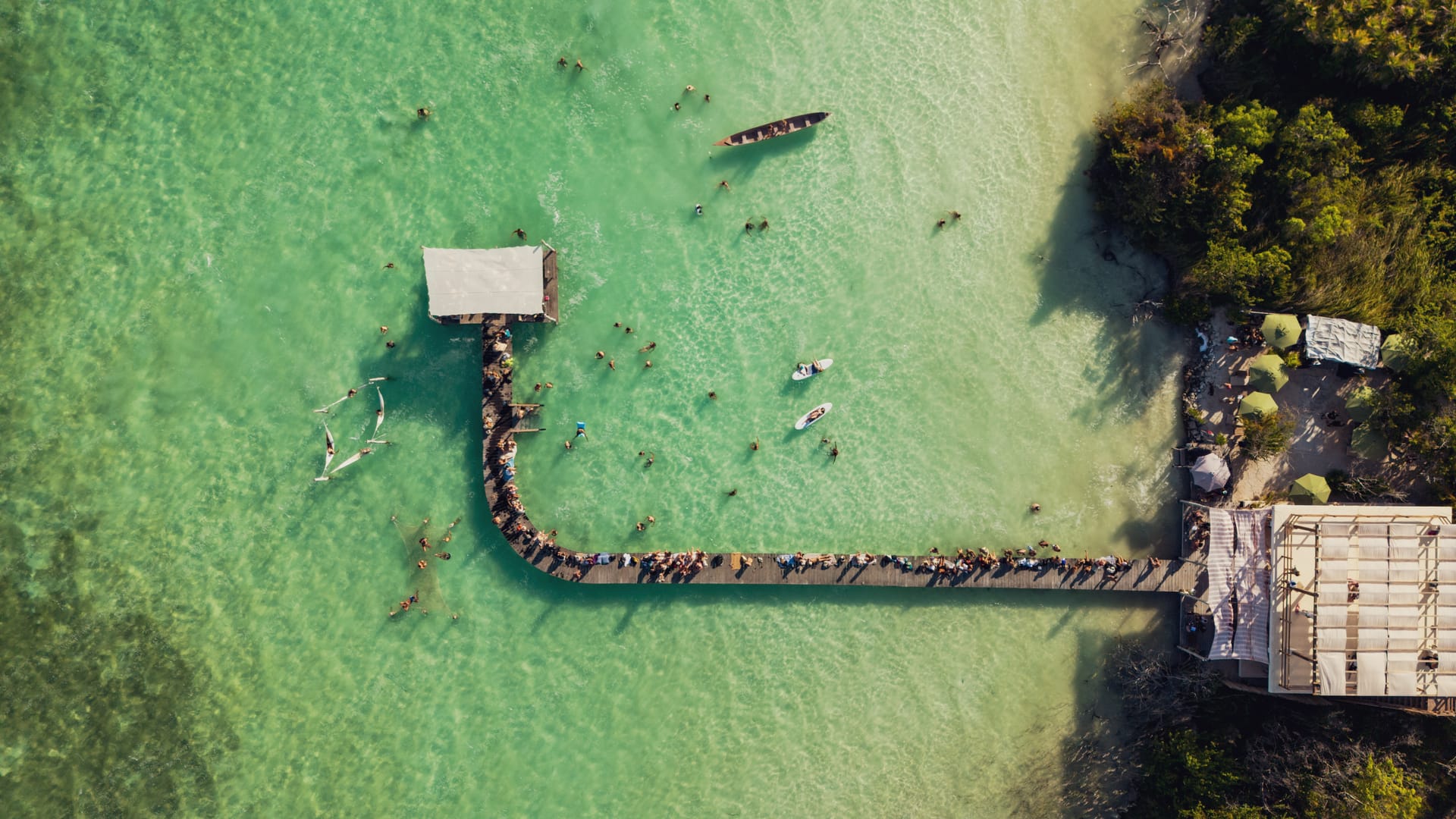 NEEK Tulum lagoon club — people gathered under palapa by the water